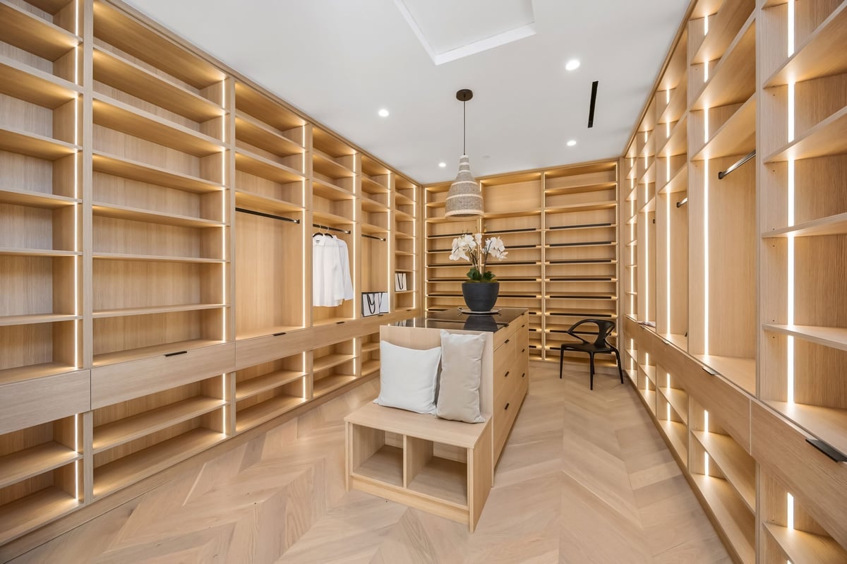 A spacious modern walk-in closet with wooden shelves, elegant lighting, and a central island bench